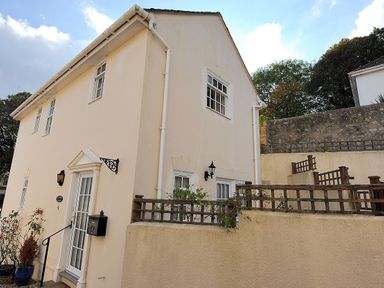 A beige two-story house with white framed windows and a small garden area surrounded by a low wall at Blacksmiths Cottage in Lyme Regis