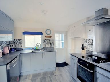 A kitchen with grey cabinets a stove a sink and a door at 1 Cobb View in Lyme Regis
