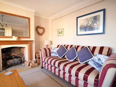 A living room with a striped sofa and cushions next to a fireplace with a wooden mantle at 1 Cobb View in Lyme Regis