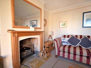 A living room with a striped sofa pillows a wooden fireplace and framed pictures at 1 Cobb View Lyme Regis