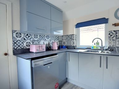 A kitchen with blue cabinets a dishwasher a sink window and pink toaster and kettle at 1 Cobb View Lyme Regis