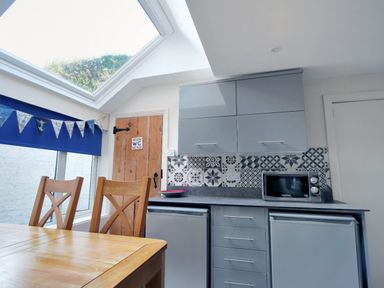 A kitchen with wooden chairs a wooden door with a wc sign gray cabinets and a microwave at 1 Cobb View Lyme Regis