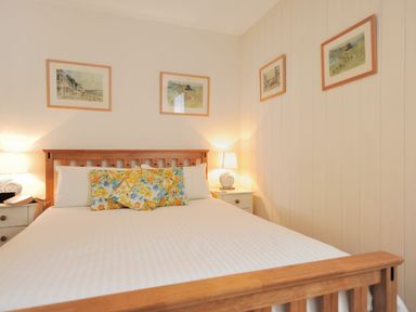 A bedroom with a wooden bed frame white bedding floral pillows two bedside tables with lamps and framed pictures on the walls at 1 Cobb View in Lyme Regis