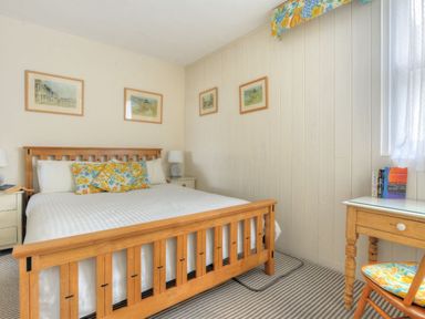 A bedroom with a wooden bed frame two bedside tables a desk and chair with floral cushions and framed pictures on the wall at 1 Cobb View in Lyme Regis