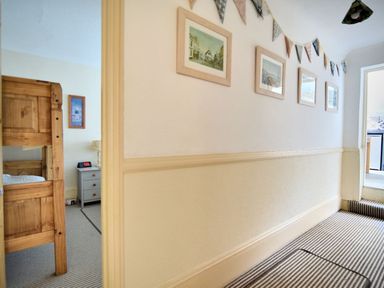 A hallway with framed pictures on the wall a striped carpet and a glimpse of a bedroom with bunk beds at 1 Cobb View Lyme Regis