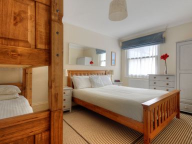 A bedroom with a double bed wooden bunk bed two bedside tables a dresser and a window at 1 Cobb View in Lyme Regis