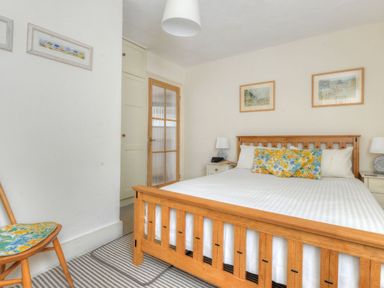 A bedroom with a wooden bed frame floral pillows two bedside tables with lamps and framed pictures on the wall at 1 Cobb View Lyme Regis