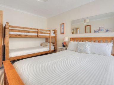 A bedroom with a double bed and wooden bunk beds with a nightstand and lamp at 1 Cobb View in Lyme Regis