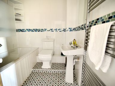 A bathroom with a bathtub a toilet a pedestal sink a towel on a heated rack and tiled floor and walls at 1 Cobb View Lyme Regis