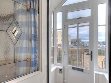 A white glass front door with side and top windows looking out to a street with buildings and parked cars at 1 Cobb View in Lyme Regis