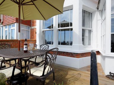 An outdoor patio with a metal table and chairs under a large umbrella and a bottle with glasses on the table at 1 Cobb View in Lyme Regis