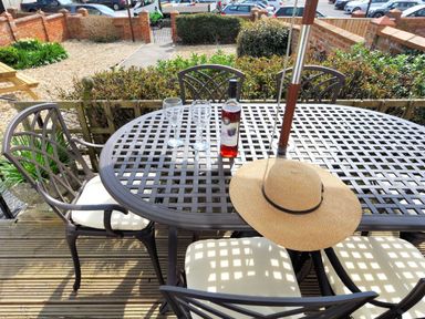 A patio table with four chairs two wine glasses a bottle and a hat on a deck outside 1 Cobb View Lyme Regis