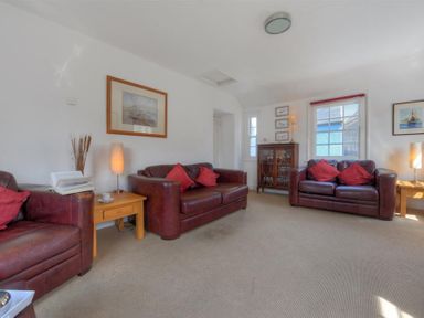 A living room with brown leather sofas red cushions wooden side tables lamps framed pictures and a wooden cabinet at Riverview in Lyme Regis