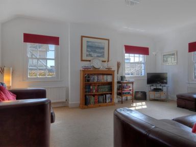 A living room with leather sofas bookshelf a television and windows with red blinds at Riverview Lyme Regis