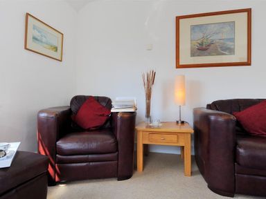 A living room with two brown leather armchairs with red cushions a wooden side table between them with a lamp and a vase and two framed pictures on the walls at Riverview in Lyme Regis