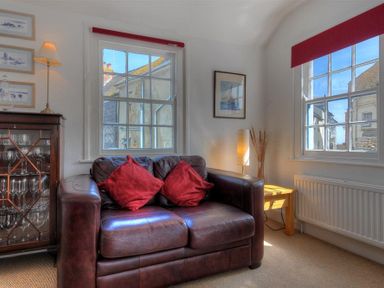 A brown leather sofa with red cushions between two windows in a sitting room at Riverview in Lyme Regis