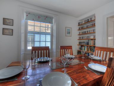 A dining room with wooden table set with plates and glasses near a window and bookshelf at Riverview in Lyme Regis