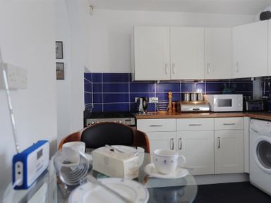 A kitchen with white cabinets blue tiled backsplash and a glass table with cups and plates at Riverview in Lyme Regis
