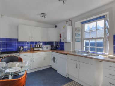 A kitchen with white cabinets, blue tiled backsplash, a glass table with chairs, and appliances including microwave and washing machine at Riverview in Lyme Regis
