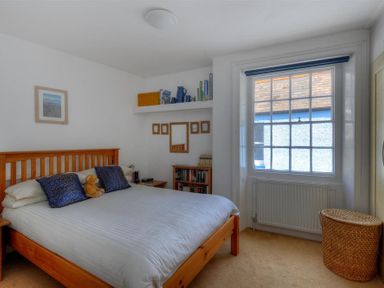 A bedroom with a wooden bed frame two pillows a teddy bear a window a shelf with books and decorative items and a wicker basket at Riverview in Lyme Regis