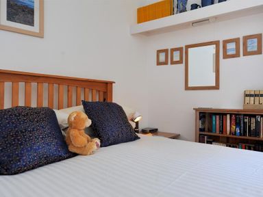 A bedroom with a wooden bed frame a teddy bear on the bed and bookshelves in Riverview Lyme Regis