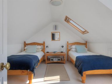 A bedroom with two single beds with blue blankets and a wooden bedside table with lamps and a radio at Riverview Lyme Regis