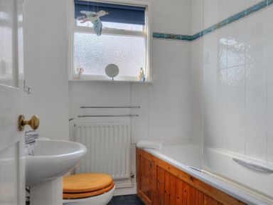 A bathroom with a sink toilet with wooden seat bathtub with wooden panel and small window at Riverview in Lyme Regis