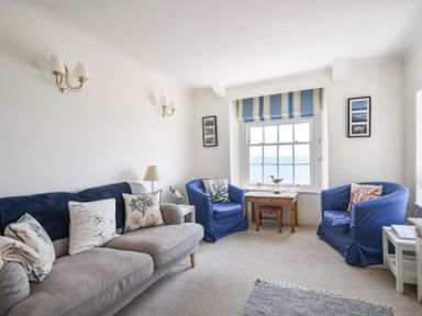 A living room with a grey sofa and blue armchairs near a window with striped blinds and a wooden table at 3 Argyle House in Lyme Regis
