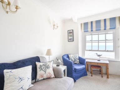 A sitting room with a gray sofa and blue armchair near a window overlooking the sea at 3 Argyle House in Lyme Regis