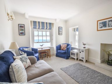 A living room with blue armchairs a beige sofa and a window with a sea view at 3 Argyle House in Lyme Regis