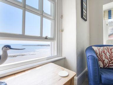 A window overlooking a beach with a wooden table and blue upholstered chair at 3 Argyle House in Lyme Regis