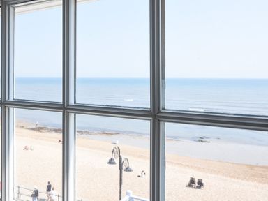 A view through a window showing a sandy beach with people and the sea at 3 Argyle House in Lyme Regis