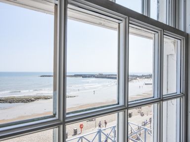 A view of a beach and seawall through a window with white frames at 3 Argyle House in Lyme Regis