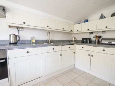 A kitchen with white cabinets a stainless steel kettle a sink a toaster and kitchen utensils at 3 Argyle House Lyme Regis