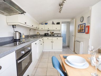 A kitchen with white cabinets gray countertop and a dining table with blue chair at 3 Argyle House in Lyme Regis