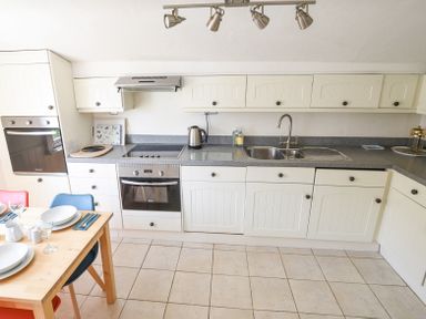 A kitchen with white cabinets grey countertops a sink stove oven kettle and a wooden dining table with plates and glasses at 3 Argyle House in Lyme Regis