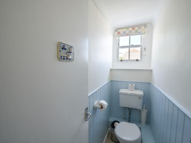 A small bathroom with a toilet a window a toilet paper holder and a toilet brush at 3 Argyle House in Lyme Regis