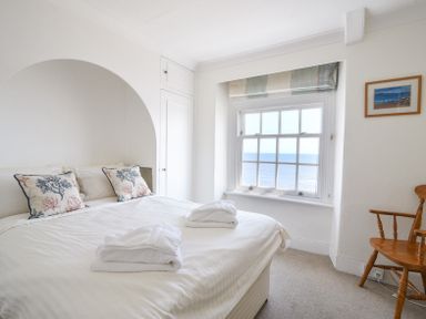 A bedroom with a bed two pillows a window with ocean view and a wooden chair at 3 Argyle House in Lyme Regis