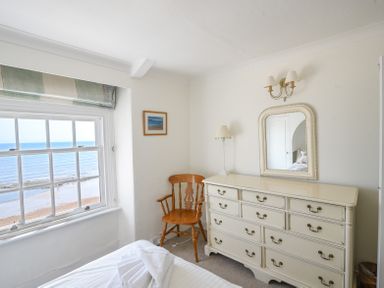 A bedroom with a wooden chair dresser with mirror and a window showing a sea view at 3 Argyle House in Lyme Regis