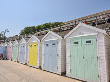 A row of small beach huts with pastel colored doors on a paved path at 3 Argyle House in Lyme Regis
