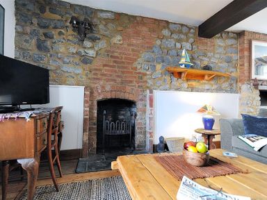 A living room with stone and brick walls a wooden table with fruit and a television on a desk at Bedrock in Lyme Regis