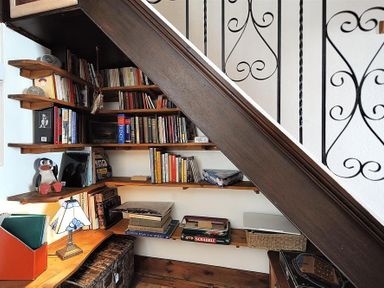 A built in bookshelf under a staircase with books a lamp and board games at Bedrock in Lyme Regis