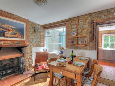 A dining area with a wooden table set with plates and wine glasses a fireplace a wooden chair and stone walls at Bedrock in Lyme Regis