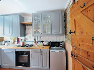 A kitchen with gray cabinets a gas stove an oven a microwave a toaster and wooden door at Bedrock in Lyme Regis