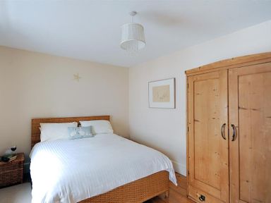 A bedroom with a wicker bed, wooden wardrobe, side table with books and a glass, and a framed picture on the wall at Bedrock in Lyme Regis