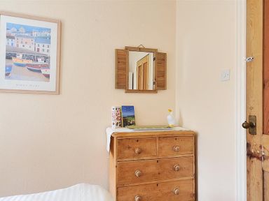 A wooden chest of drawers with books and a duck figurine on top a mirror on the wall and a framed picture of boats on the wall at Bedrock in Lyme Regis