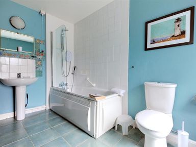 A bathroom with a bathtub shower sink toilet small stool and framed picture on blue wall at Bedrock in Lyme Regis