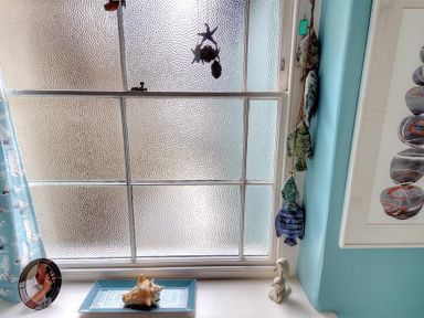 A window with frosted glass and a windowsill with a shell on a tray a small sculpture and hanging fish decorations at Bedrock in Lyme Regis