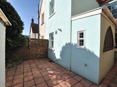 A small paved courtyard with a blue building wall and a brick fence with some plants at Bedrock in Lyme Regis