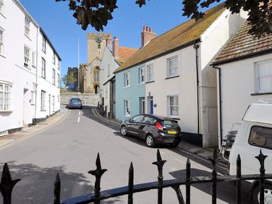A street with parked cars and rows of houses with a church in the background at Bedrock in Lyme Regis